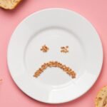 Prato branco com grãos formando um rosto triste, simbolizando a relação difícil com a comida e o transtorno alimentar