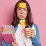 Mulher jovem com expressão de surpresa, segurando café e papéis, coberta por post-its, representando desorganização e sobrecarga, um dos desafios do TDAH em adultos.