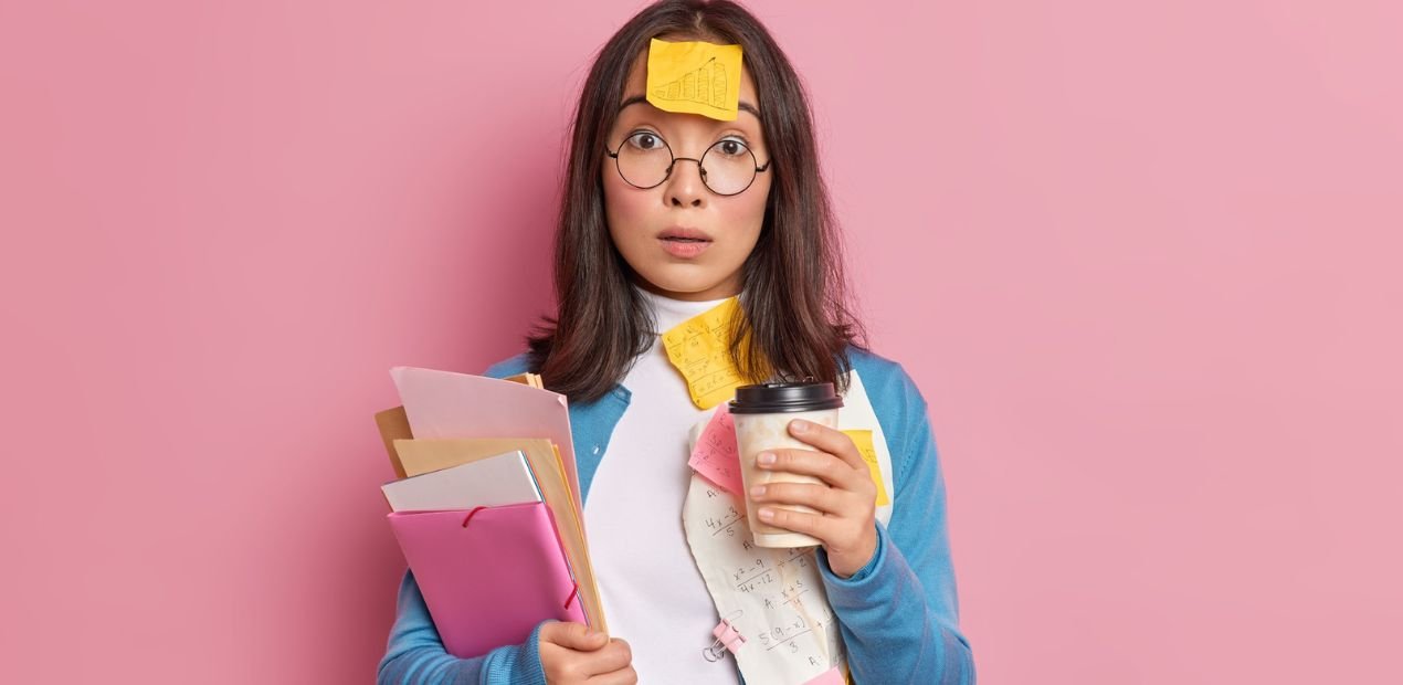 Mulher jovem com expressão de surpresa, segurando café e papéis, coberta por post-its, representando desorganização e sobrecarga, um dos desafios do TDAH em adultos.