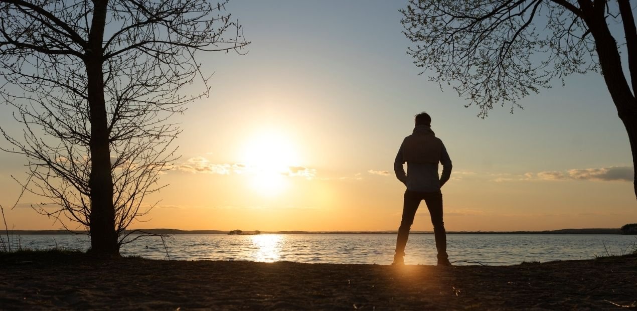 Silhueta de homem em pé diante do pôr do sol, simbolizando introspecção e sintomas da depressão masculina