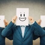 Homem bipolar no relacionamento ilustrado por três figuras idênticas vestindo terno azul, cada uma segurando uma folha com rosto desenhado — um triste, um feliz e um irritado — simbolizando as oscilações de humor típicas do transtorno bipolar.