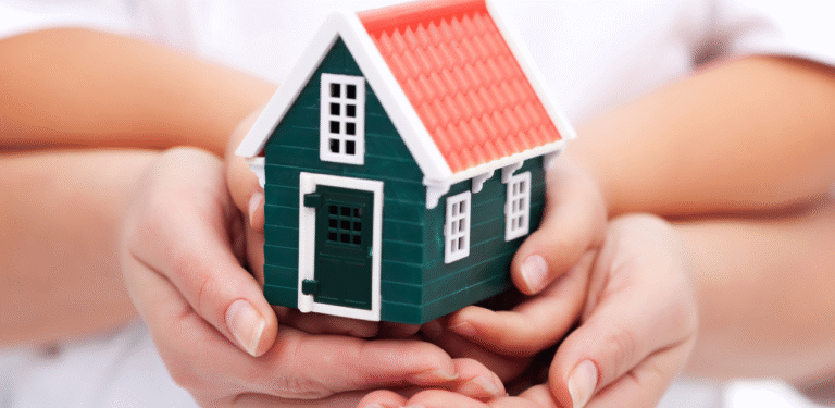 Casa em miniatura sendo segurada por duas mãos, representando segurança, acolhimento e a busca por um lar que vai além do status social