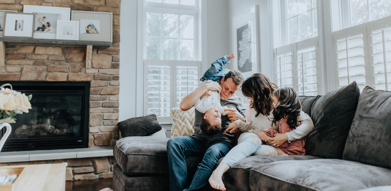 Família sentada no sofá em um momento de afeto e descontração, simbolizando bem-estar emocional e a importância do lar como espaço de conexão