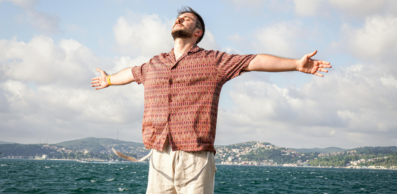 Homem de braços abertos diante do mar simbolizando bem-estar psicológico e sensação de liberdade