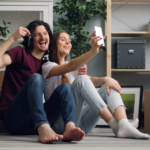 Casal sentado no chão entre caixas de mudança, sorrindo em um novo lar, simbolizando renovação emocional e bem-estar familiar
