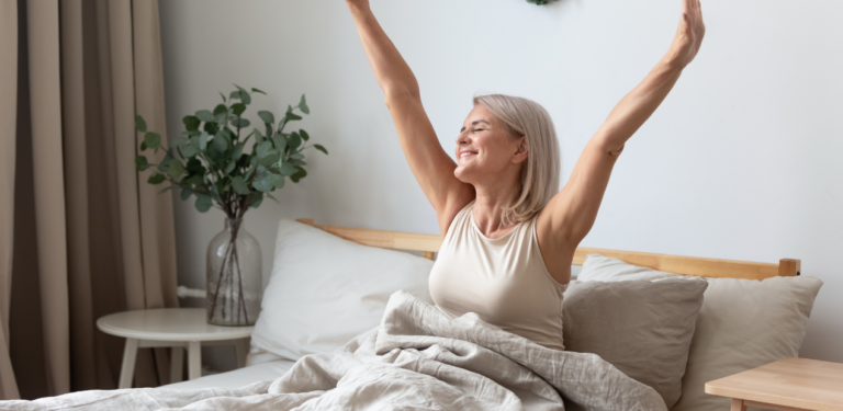 Mulher acordando em um quarto iluminado, alongando os braços, simbolizando bem-estar mental e renovação em um ambiente acolhedor