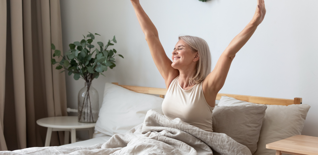 Mulher acordando em um quarto iluminado, alongando os braços, simbolizando bem-estar mental e renovação em um ambiente acolhedor