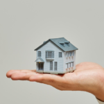 Mão segurando uma miniatura de casa, simbolizando a escolha consciente do lar e o impacto do ambiente na saúde mental