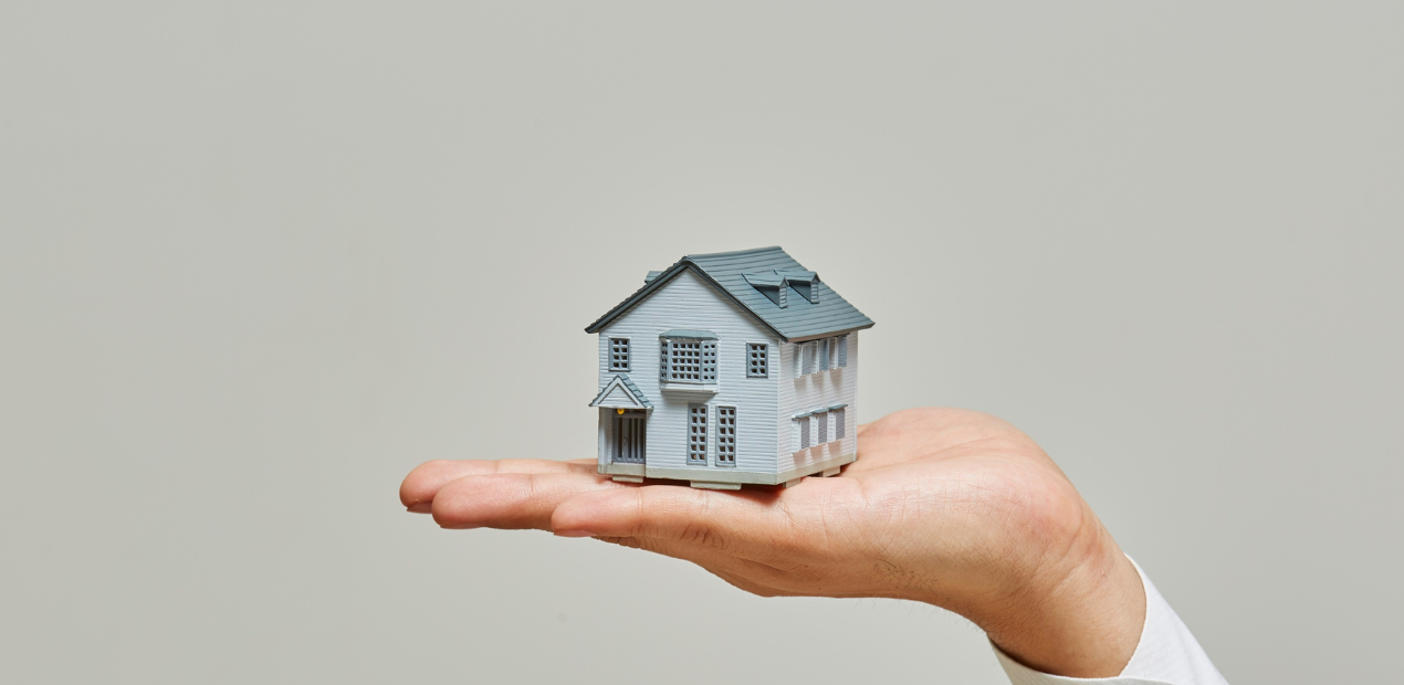 Mão segurando uma miniatura de casa, simbolizando a escolha consciente do lar e o impacto do ambiente na saúde mental