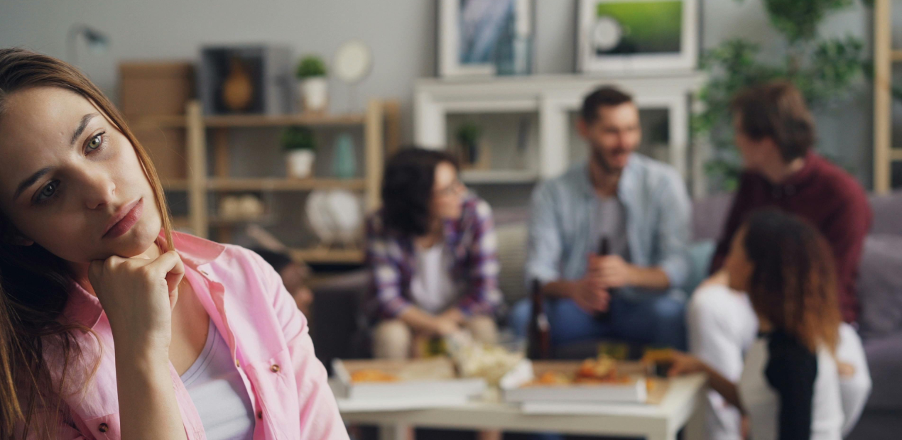 Isolamento emocional em meio a outras pessoas Mulher com expressão distante em primeiro plano enquanto grupo social interage ao fundo, sugerindo isolamento emocional