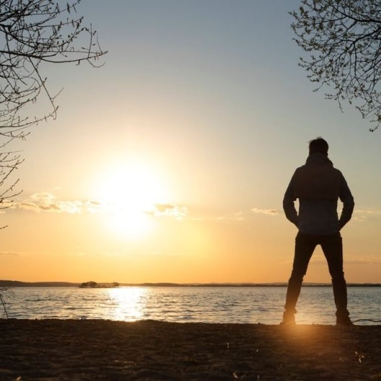 Silhueta de homem em pé diante do pôr do sol, simbolizando introspecção e sintomas da depressão masculina