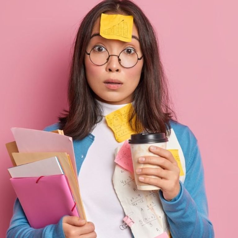 Mulher jovem com expressão de surpresa, segurando café e papéis, coberta por post-its, representando desorganização e sobrecarga, um dos desafios do TDAH em adultos.
