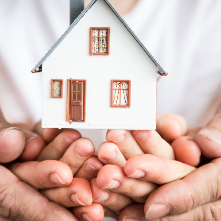 Mãos de adultos e crianças segurando uma miniatura de casa, simbolizando proteção, segurança emocional e bem-estar familiar