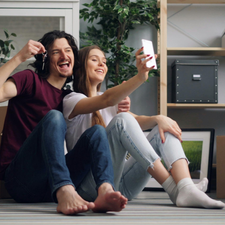 Casal sentado no chão entre caixas de mudança, sorrindo em um novo lar, simbolizando renovação emocional e bem-estar familiar